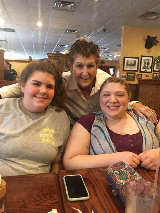 Three friends sit together at a table, smiling and enjoying a casual lunch at a warm restaurant.