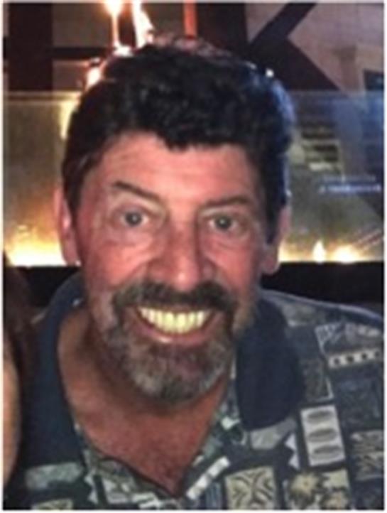 A cheerful man with facial hair is smiling warmly at a gathering in a lively bar ambiance.