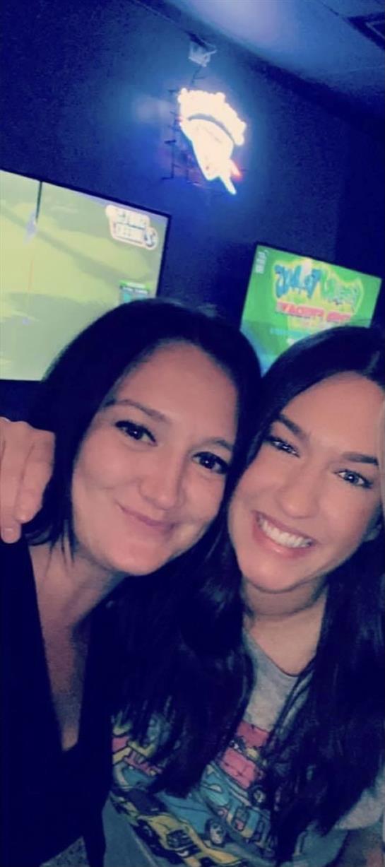 Two friends embrace and smile happily while enjoying a fun night out at an entertainment venue.