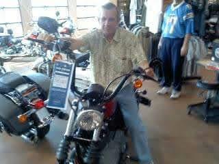Man poses on a motorcycle in a store, browsing available accessories and apparel nearby.