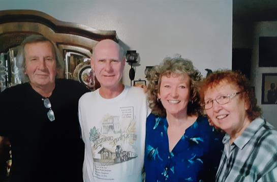 Four friends share laughter and smiles during a joyful reunion in a warm, inviting space.