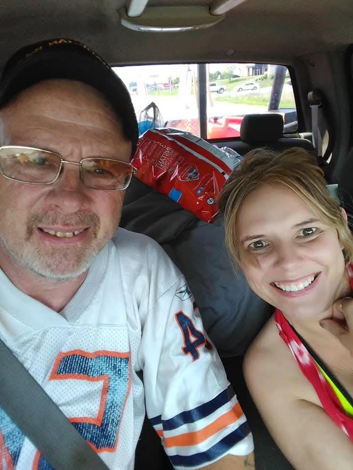 Man and woman share smiles inside a truck while parked at a roadside stop on a sunny day.
