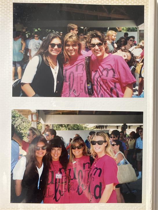 Friends pose happily together wearing matching shirts at a vibrant outdoor festival.