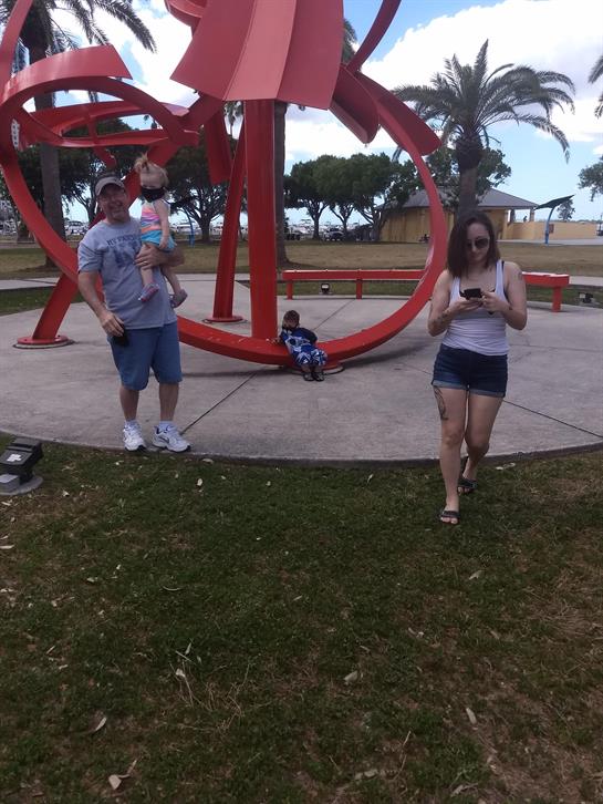 A family enjoys a bright day at the park, with a child playing near a colorful art installation.