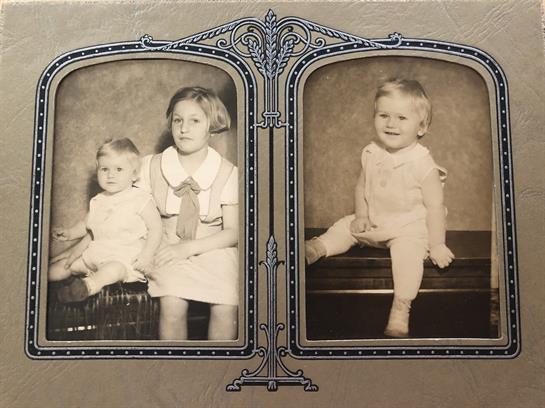 Two young children sit for a formal portrait in classic attire in an old studio.