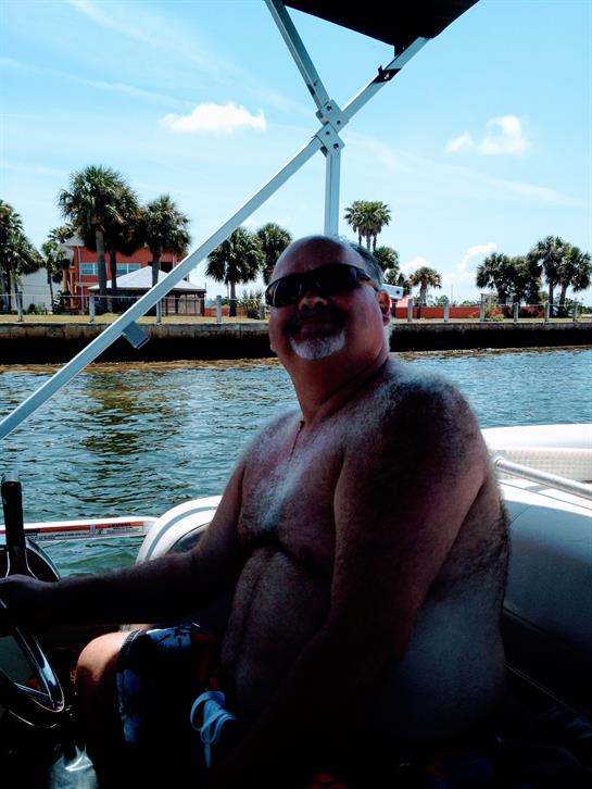 Man relaxes and enjoys steering a boat on a bright, sunny day near palm trees.