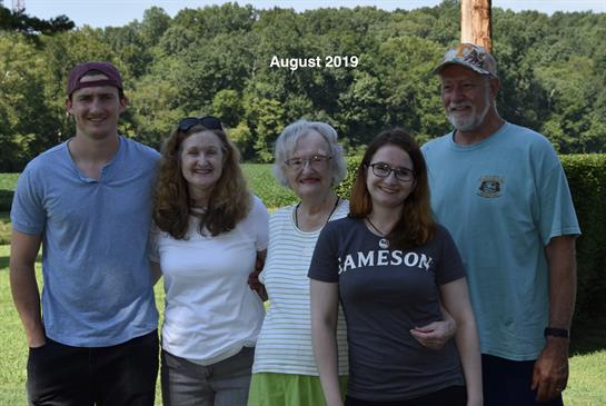 Friends and family stand together outdoors, enjoying a summer gathering in a scenic landscape.