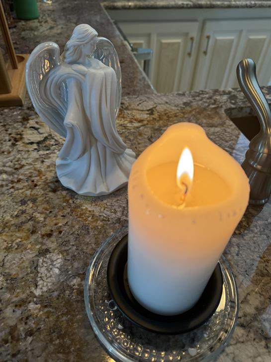 A lit candle casts a gentle glow next to a serene angel statue on a marble countertop.