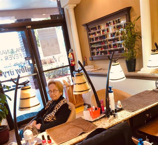 A senior woman relaxes in a nail salon, savoring the bright afternoon light.
