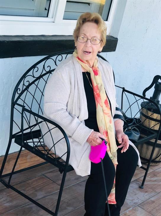 An elderly woman enjoys the outdoors on a bench, holding a pink dog leash and looking surprised.