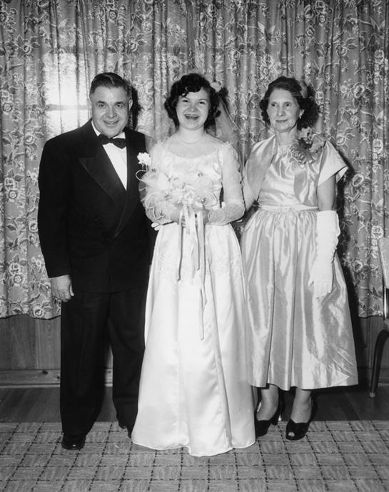 A couple in formal attire stands with a friend in an elegant gown at a wedding.