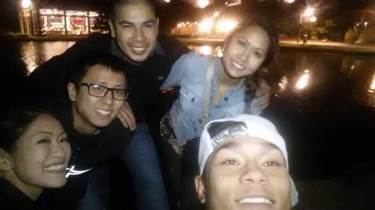Four friends smile together at night by the water, lit up by city lights.