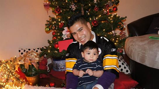 A joyful father holds his baby while sitting by a beautifully illuminated Christmas tree.