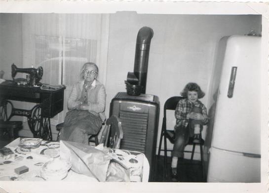 An elderly man and woman sit in a cozy room alongside a child, surrounded by retro appliances.