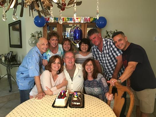 Friends and family gather around a table with birthday cakes to celebrate.