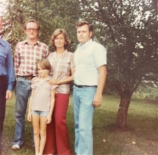 A family poses together in a green garden filled with trees, smiling cheerfully.