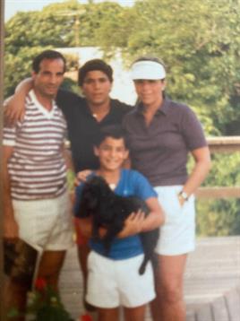 Four family members enjoy a sunny day outdoors with a dog in a green setting.