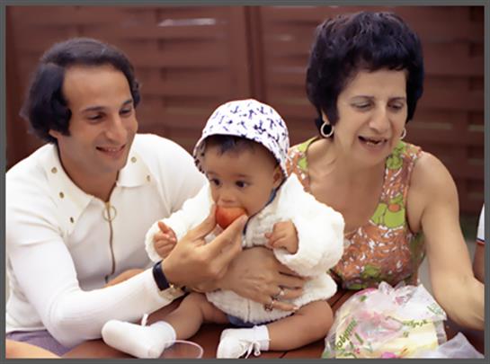 A couple lovingly feeds their baby while enjoying a gathering with smiles and happiness.