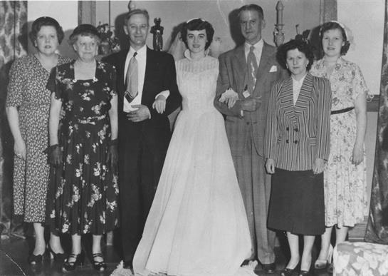 A bride stands in a wedding dress with family members, all dressed formally at a reception venue.