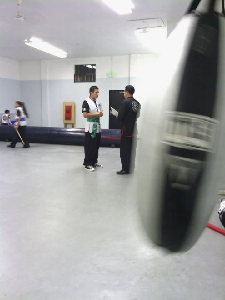 Two martial artists engage in conversation while others practice their techniques in the background.