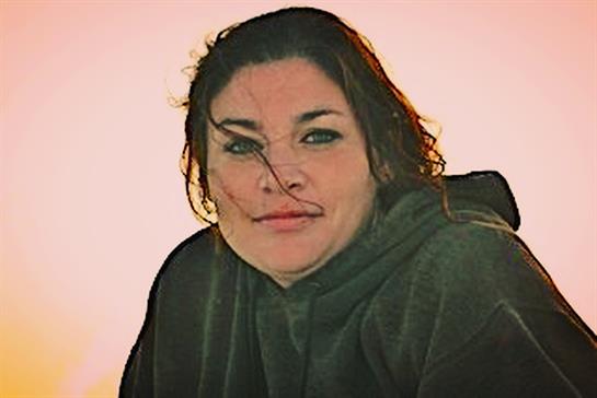 A woman smiles as the wind tousles her hair while watching the sunset by the beach.