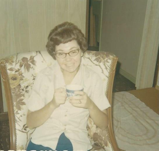 Older woman in a cozy armchair smiles warmly while holding a cup at home.