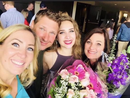 Friends celebrate together, smiling warmly while holding colorful flower bouquets at an event.