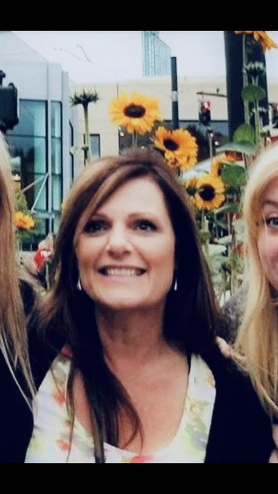 Three friends smile brightly in front of colorful sunflowers during a joyful outdoor event.