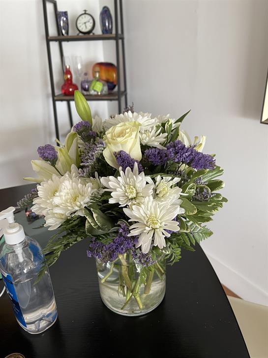 Fresh flowers in a clear vase, featuring white and purple blooms, displayed on a table.