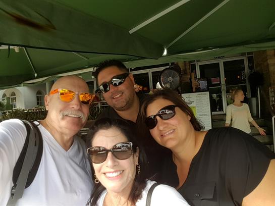 Four friends smile together under a green canopy while spending time at a cafe during the afternoon.