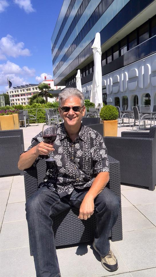 Individual relaxes outdoors, sipping red wine while seated in a stylish modern setting.
