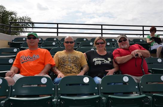 Friends relax on stadium seats, wearing team colors and sunglasses, waiting for the game to begin.