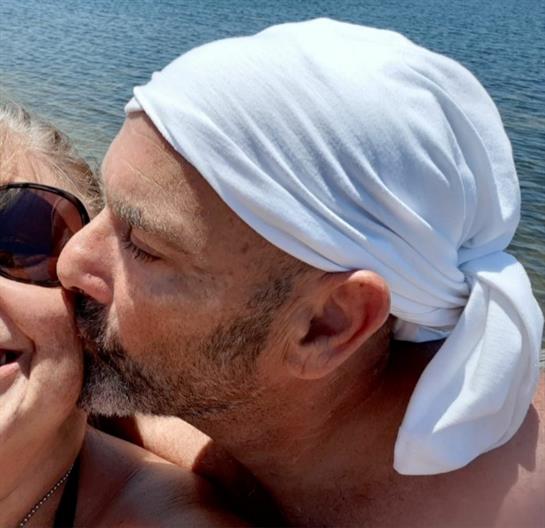 Man kisses woman while both smile together by the water in a serene coastal setting.