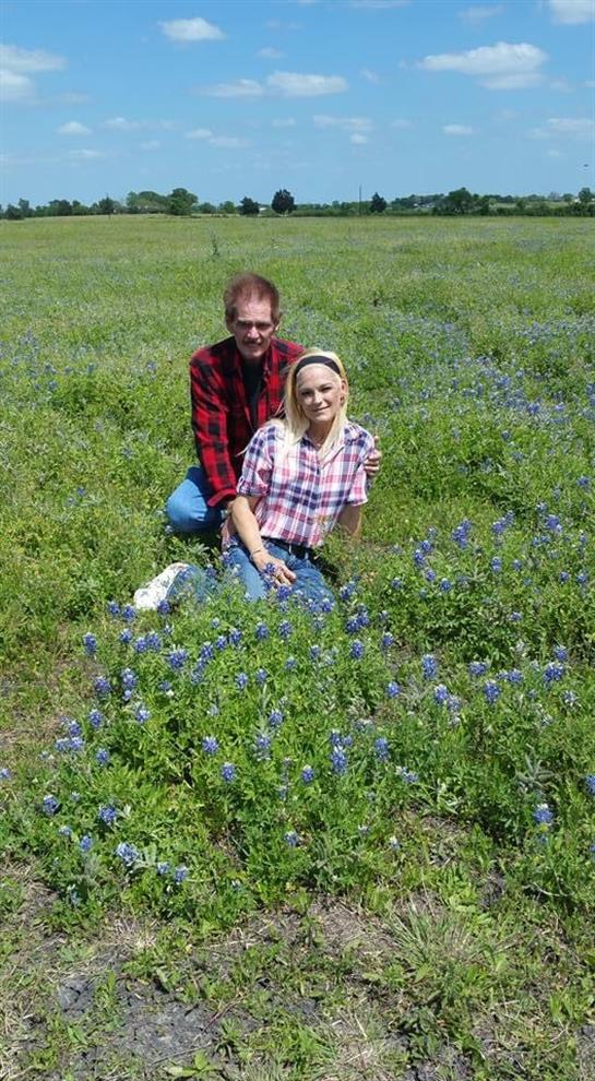 A couple kneels together in a vibrant field of bluebonnets, enjoying the warm sunshine.