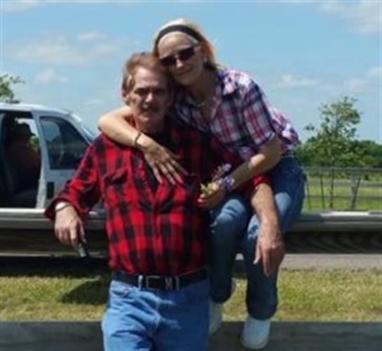 Two people are smiling and posing happily together outdoors under a clear blue sky.