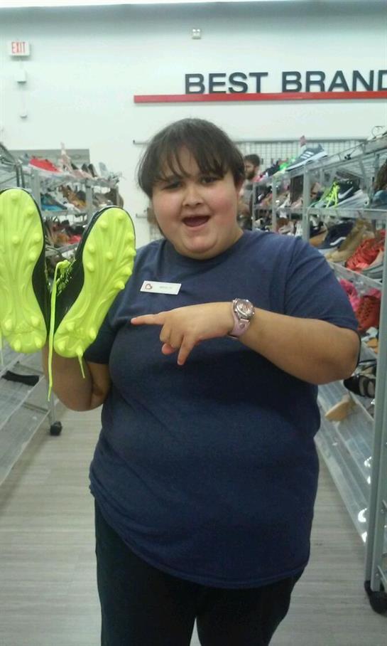 Individual shows off vibrant yellow footwear while smiling in a retail store aisle.