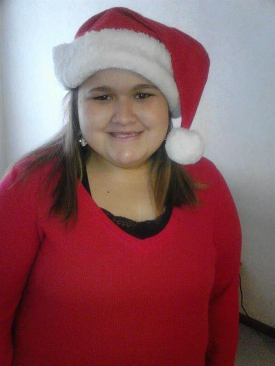 Young girl in a bright red sweater and Santa hat smiles happily while celebrating Christmas.