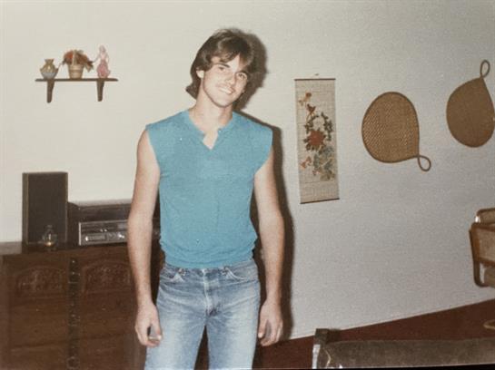A young man poses confidently in a relaxed outfit amid nostalgic home decor.