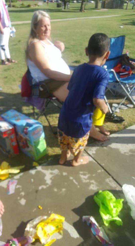 Kids are playing in water while families relax on chairs at a sunny summer gathering in the park.