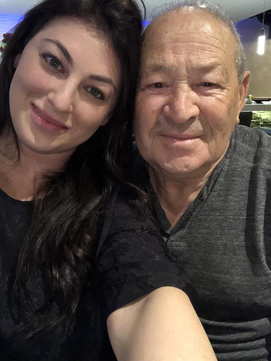 Two people share a close and happy moment, smiling and looking at the camera in a warm setting.