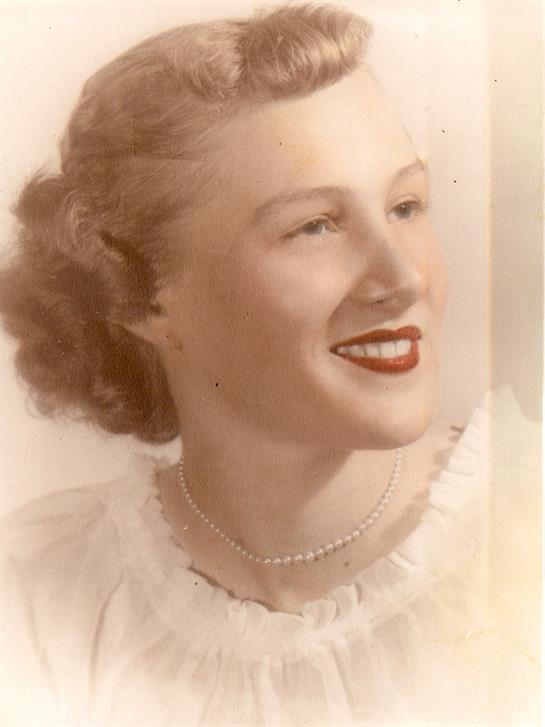A woman smiles warmly, showcasing vintage fashion and elegant pearl jewelry with soft curls.