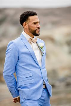 A groom showcases his stylish light blue suit while awaiting his bride at a coastal wedding.