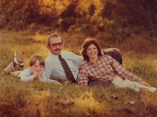 A family relaxes on the grass in a park, smiling and enjoying quality time together.