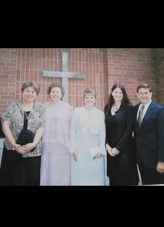 Group of five individuals dressed in formal clothing at a church event near a cross.