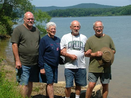 Friends stand together by the lake, sharing smiles and laughter on a warm summer day.