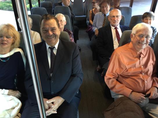Group of well-dressed individuals sits on a bus, engaged in conversation and enjoying the ride.