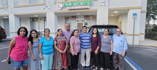 Friends gather for a joyful celebration outside an Indian cuisine restaurant at sunset.
