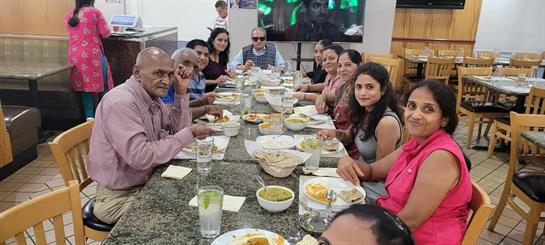Friends and family sit together sharing food and laughter at a restaurant in a festive atmosphere.