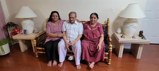 Three adults smile together on a home bench, enjoying each other's company.