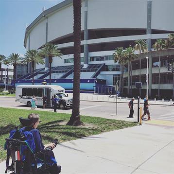 A person in a wheelchair relaxes under the sun while observing activity around a stadium.